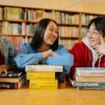 Nowoczesna biblioteka szkolna: jak stać się centrum kompetencji informacyjnych i medialnych? Troje uczniów różnych narodowości śmieje się i uczy razem w bibliotece