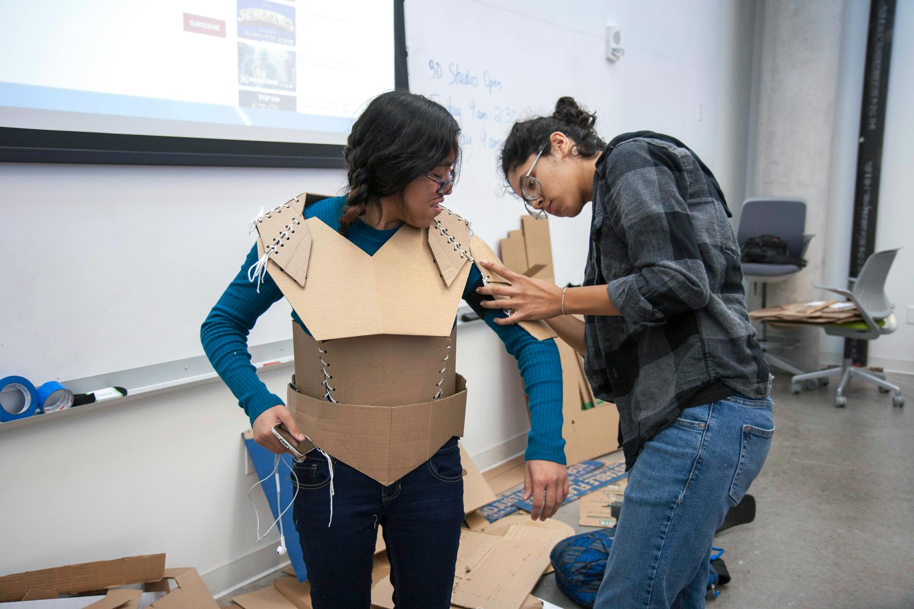 Dwóch studentów tworzy tekturową zbroję na zajęciach projektowych