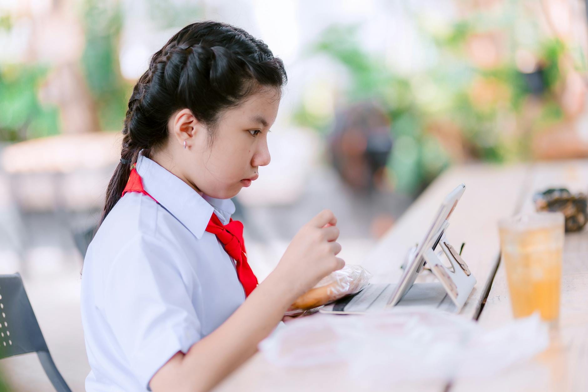 Uczennica w mundurku uczy się na tablecie w kawiarni na świeżym powietrzu